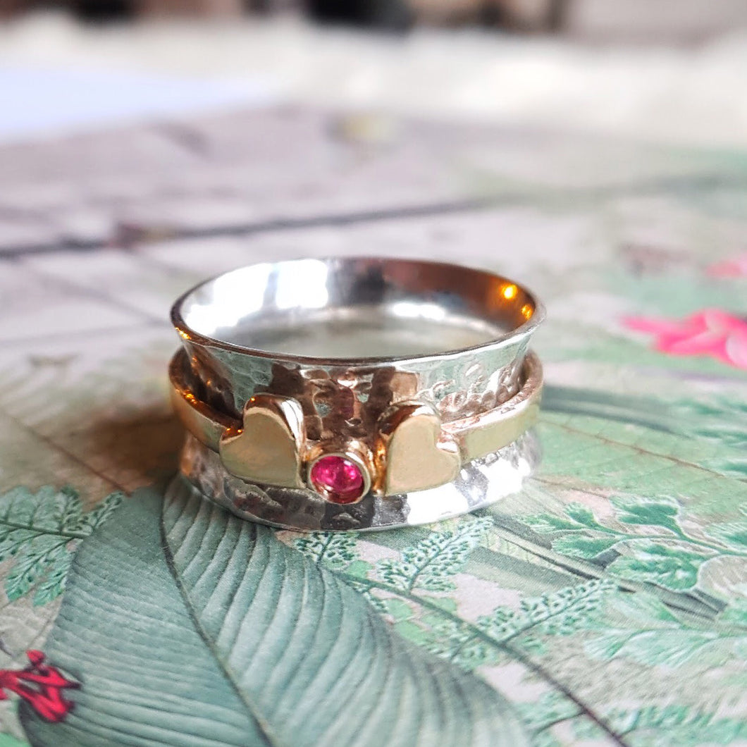 Spinning ring with two gold hearts surrounding gemstone